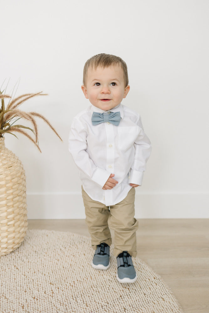 Dusty pre-tied bow tie worn by a young boy wearing white shirt, tan pants and gray shoes.
