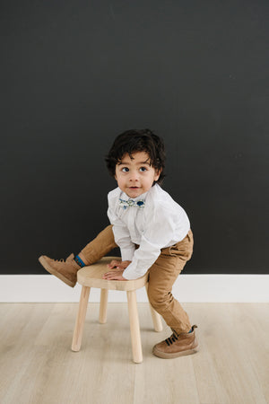 Frisco pre-tied bow tie on a young boy wearing a white shirt, tan pants and brown shoes. 