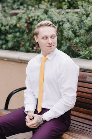 Golden tie worn with a white shirt and plum purple pants.