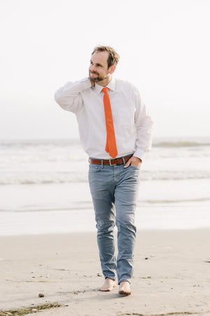 Tangerine tie worn with a white shirt and blue pants.