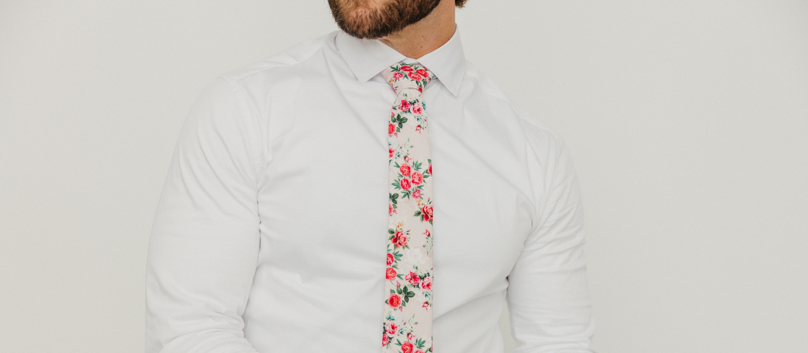 Picture of a man wearing a white long sleeve dress shirt and a colorful floral necktie called "Rose Garden".