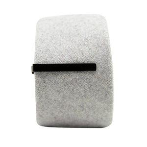 Solid black metal tie bar clipped onto a gray textured wool tie that is rolled up.