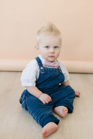 Blush Pre-Tied Bow Tie worn by baby with white shirt and blue denim overalls. 