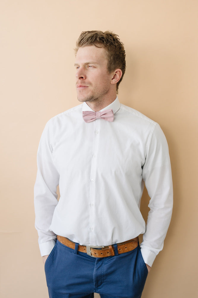 Blush Pre-Tied bow tie worn with a white shirt, brown belt and blue pants. 