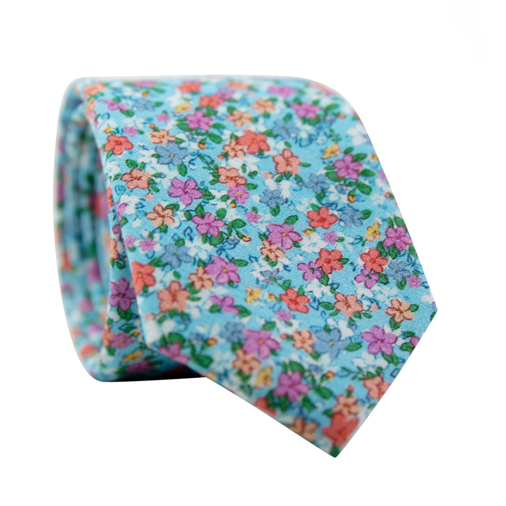 Dahlia Skinny Tie. Light blue background with a variety of small pink, red, salmon and white flowers and green leaves. 
