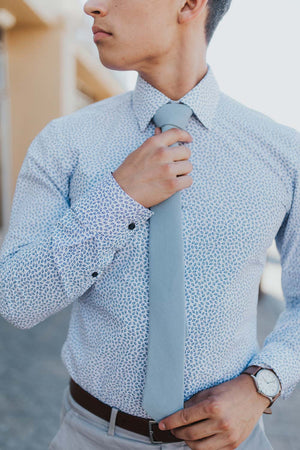 Dusty tie worn with a blue patterned shirt, brown belt and light gray pants.