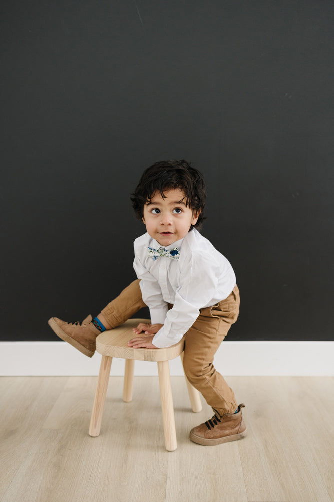 Frisco pre-tied bow tie on a young boy wearing a white shirt, tan pants and brown shoes. 