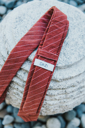 Garnet tie sitting on rocks showing the DAZI label logo on back.