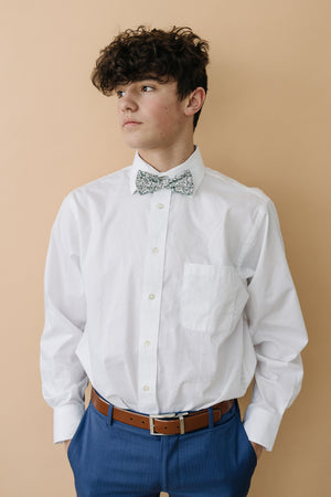 Hidden Garden pre-tied bow tie worn with a long sleeve white shirt, brown belt and blue pants.