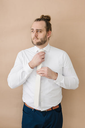 Ivory tie worn with a white shirt, brown belt and navy blue pants.