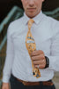 Marigold tie worn with a white shirt, brown belt and gray patterned pants.