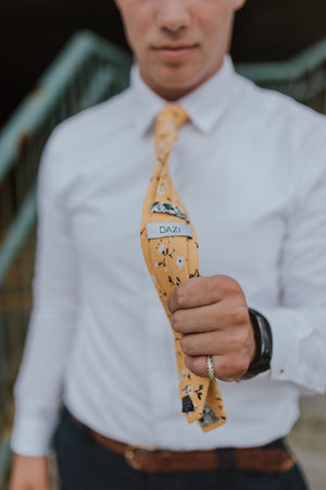 Marigold tie worn with a white shirt, brown belt and gray patterned pants.