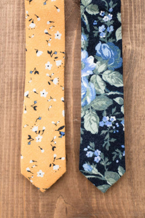 Marigold tie laying on a piece of wood next to another floral tie.