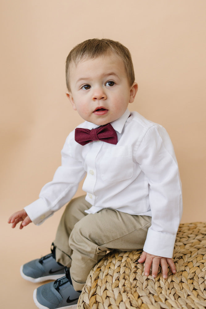 Merlot pre-tied bow tie worn by a young boy in a white shirt and tan pants. 