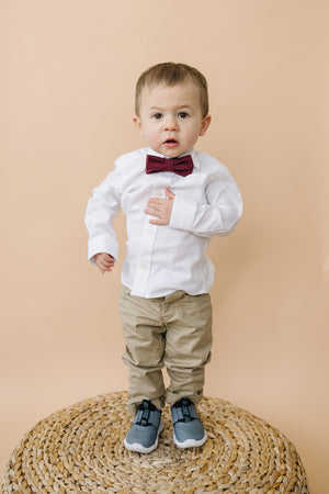 Merlot pre-tied bow tie worn by a young boy in a white shirt and tan pants. 