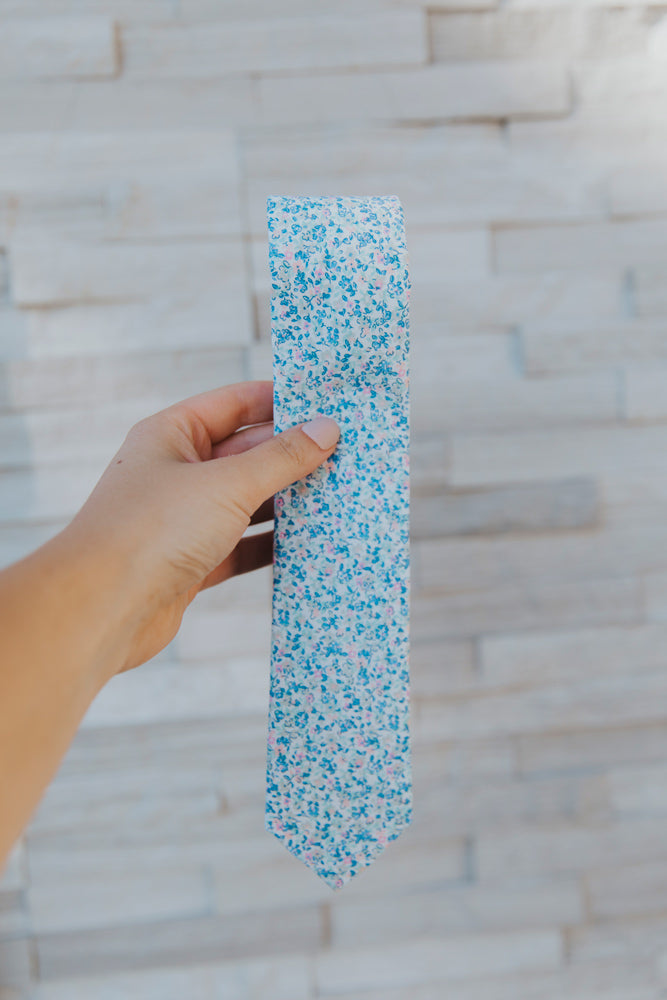 Misty Love tie being held up in front of a white brick wall.