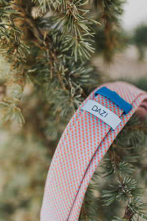 Opal tie photographed lying with the back side up showing the "DAZI" loop on the back of the tie sitting on a pine tree branch. 