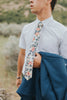 Orange Pansy tie worn with a white shirt, brown belt and royal blue suit with jacket hanging over arm.