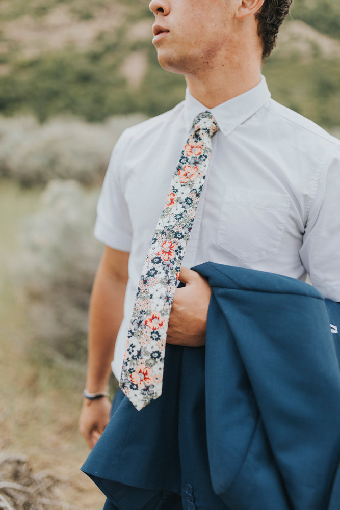 Orange Pansy tie worn with a white shirt, brown belt and royal blue suit with jacket hanging over arm.