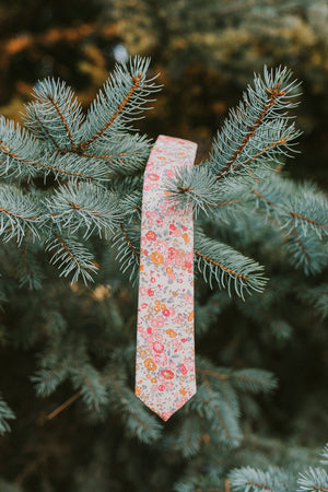 Pink Meadow tie hanging from a pine tree branch.