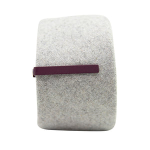 Solid plum metal tie bar clipped onto a gray textured wool tie that is rolled up.
