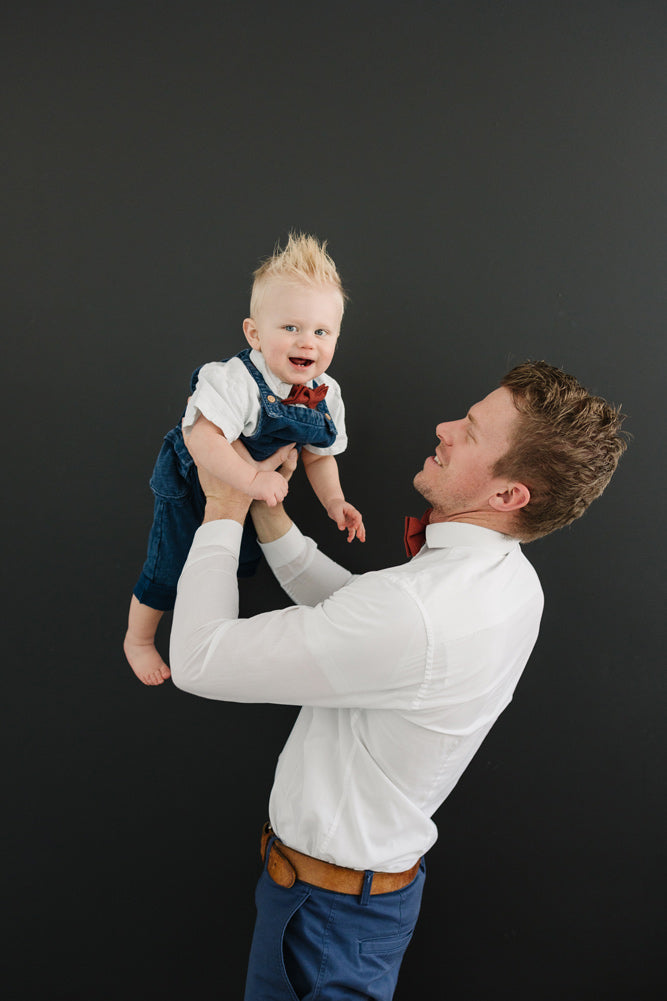 Rust pre-tied bow ties worn by father and son in white shirts and blue pants. 