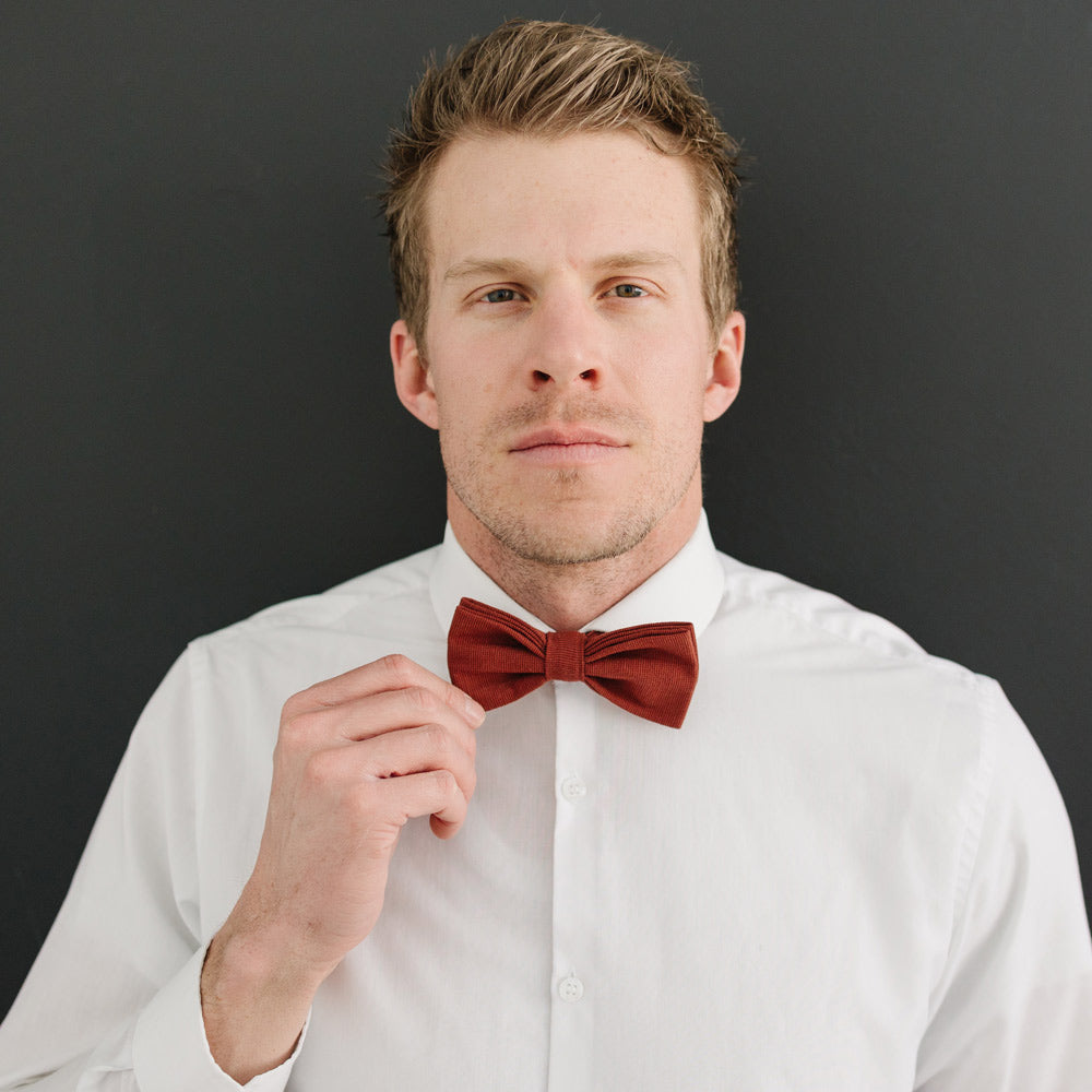 Rust pre-tied bow tie worn with a white long sleeve shirt.