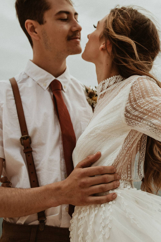 Rust tie worn with a white shirt and brown leather suspenders.