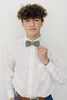 Sage pre-tied bow tie worn with a white long sleeve shirt, brown belt and blue pants. 