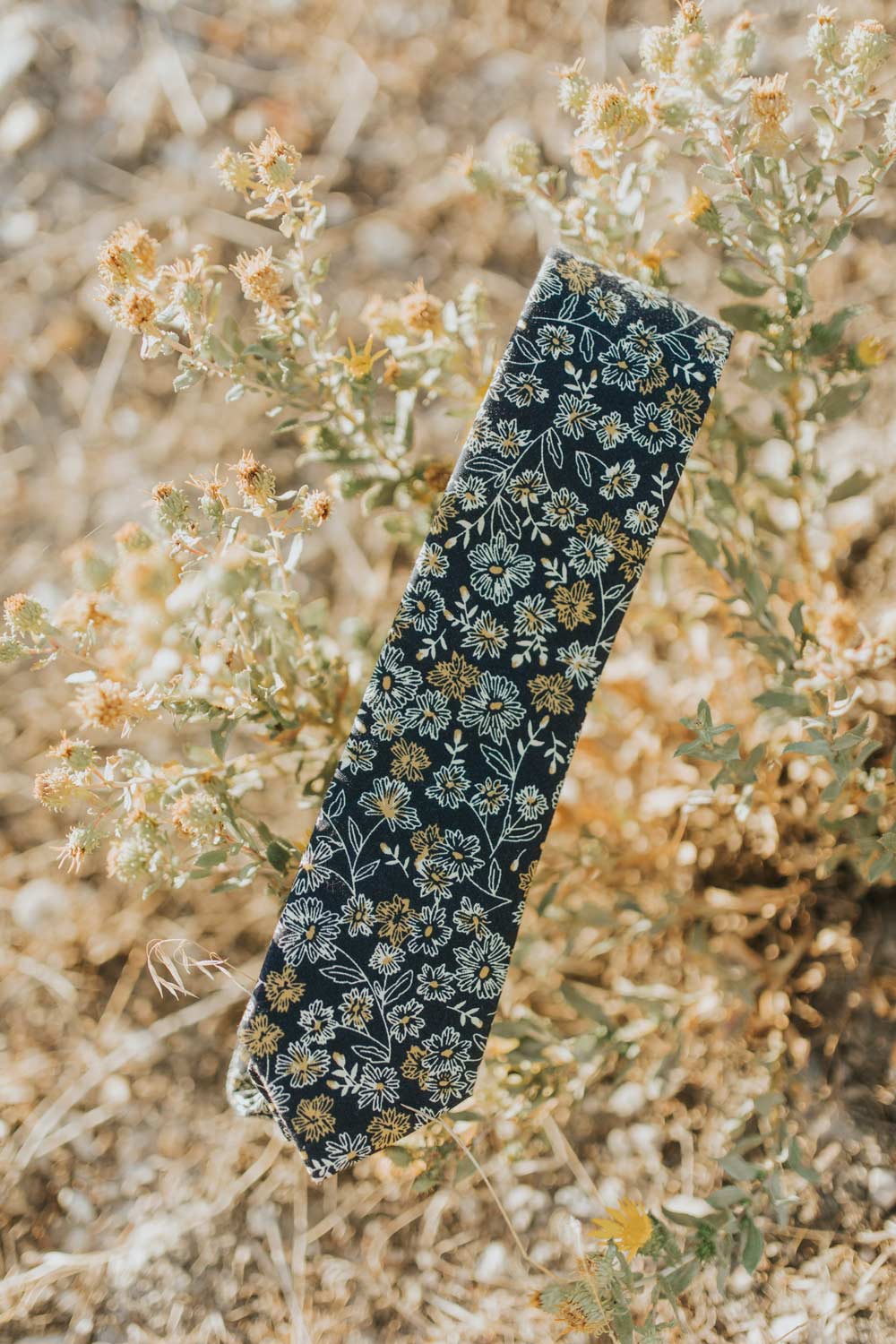 Senna floral tie photographed folded in half sitting on some green and gold flowers.