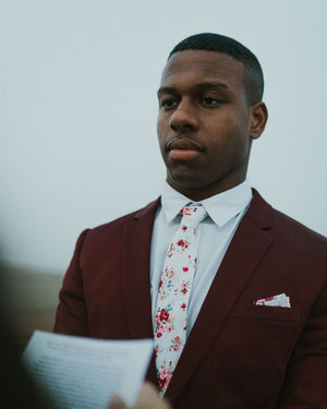 White Floral tie worn with a white shirt, burgundy red suit jacket and matching pocket square.